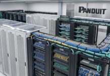 Panduit fortalece la infraestructura de conectividad para el regreso a clases Fotografía de un cuarto de telecomunicaciones moderno e iluminado que muestra múltiples racks y gabinetes de la marca Panduit. Destacan gruesos mazos de cables de red en colores azul, amarillo y verde, los cuales están peinados y organizados de manera impecable sobre bandejas horizontales. A la izquierda se aprecian pasillos contenidos con techos transparentes, y al fondo resalta un gran logotipo negro de Panduit montado sobre un panel de acabado metálico.
