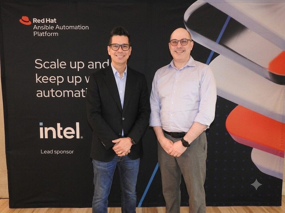 La evolución de la automatización de TI hacia modelos preventivos e inteligentes Fotografía de Daniel Romero y Chad Ferman posando de pie y sonriendo frente a un fondo negro con el logotipo de Red Hat Ansible Automation Platform y el patrocinio de Intel. Daniel viste un saco negro y jeans, mientras que Chad usa una camisa azul claro y pantalones grises.