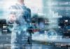 Hitachi Vantara: ¿Sabe dónde están sus datos en la era de la IA? Fotografía de un hombre de traje interactuando con una interfaz digital futurista y translúcida, la cual despliega múltiples paneles luminosos con mapas mundiales, gráficos de barras y flujos de información.