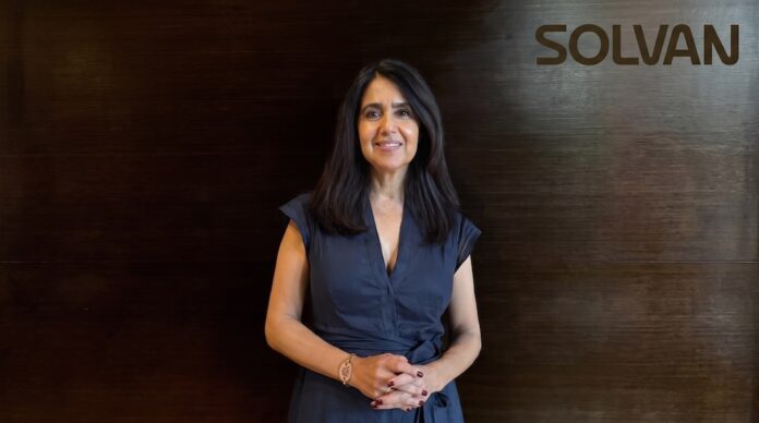modernización de infraestructura TI: Fotografía de Zadie Eternod Noriega, CEO de SOLVAN Soluciones de Vanguardia, posando de frente con una sonrisa. Ella viste un vestido azul oscuro y se encuentra de pie ante un fondo de paneles de madera oscura que muestra el logotipo de SOLVAN en la esquina superior derecha.