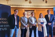 TOTVS fortalece a México como hub estratégico para su expansión en América Latina Fotografía grupal de cinco ejecutivos de TOTVS, cuatro hombres y una mujer, posando de pie y sonriendo a la cámara en un salón clásico con paredes revestidas en madera y piso de duela. A la izquierda se observa parcialmente un banner azul con el logotipo corporativo de la empresa.