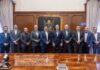 Schneider Electric amplía su manufactura en Querétaro con tres nuevas plantas Fotografía grupal de diez hombres con traje, que incluye a funcionarios del gobierno de Querétaro y directivos de Schneider Electric, posando de pie y sonriendo frente a un muro de madera adornado con el escudo oficial del estado.
