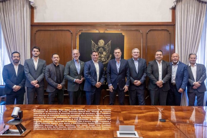 Fotografía grupal de diez hombres con traje, que incluye a funcionarios del gobierno de Querétaro y directivos de Schneider Electric, posando de pie y sonriendo frente a un muro de madera adornado con el escudo oficial del estado.