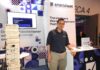 Systech Consulting impulsa la adopción de Smartsheet en América Latina Fotografía de Jorge Díaz, CEO de Systec Consulting, de pie en un módulo de exhibición de Smartsheet. A su izquierda se encuentra una torre gigante de bloques tipo Jenga de madera, donde cada pieza tiene impreso el logotipo de la marca de software.