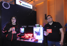 Adata revoluciona el rendimiento extremo para los entusiastas del hardware Fotografía en plano medio de Adriana Morales y Donato Moreno en el estand de ADATA y XPG, sosteniendo empaques de memorias RAM y unidades SSD de quinta generación junto a un gabinete de computadora transparente iluminado con luces LED RGB y periféricos.
