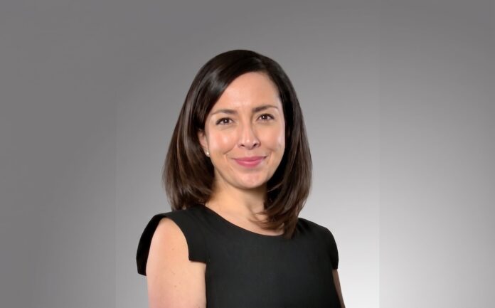 Fotografía de retrato de Carlota Blom posando de frente con una ligera sonrisa, vestida con una blusa formal de color negro y sin mangas sobre un fondo neutro en degradado gris.