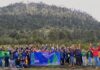 Epson México refuerza su compromiso ambiental con la restauración del Nevado de Toluca Fotografía grupal que reúne a decenas de voluntarios sonrientes alzando los brazos en una pradera al pie de una montaña arbolada, sosteniendo una lona azul con los logotipos de Epson y la leyenda "Reforestamos 2026".