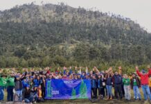 Epson México refuerza su compromiso ambiental con la restauración del Nevado de Toluca Fotografía grupal que reúne a decenas de voluntarios sonrientes alzando los brazos en una pradera al pie de una montaña arbolada, sosteniendo una lona azul con los logotipos de Epson y la leyenda "Reforestamos 2026".