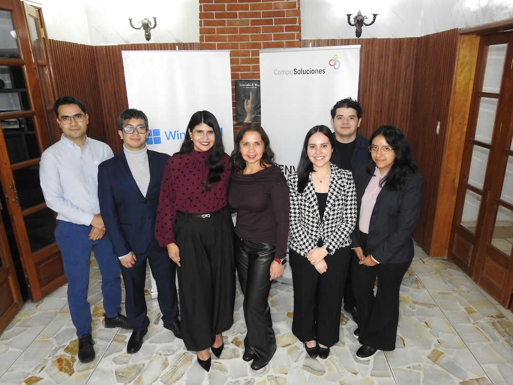 Fotografía grupal que muestra a siete profesionales de CompuSoluciones y Microsoft posando en fila frente a los páneles corporativos del evento en el vestíbulo de un inmueble.
