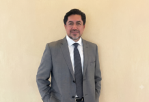 HD Latinoamérica: México celebra su identidad ¿pero qué tan protegida está la digital? Fotografía de retrato de Fausto Escobar posando de pie con las manos en los bolsillos, vistiendo un traje gris, camisa blanca y corbata azul oscuro, sobre un fondo plano de color beige claro.