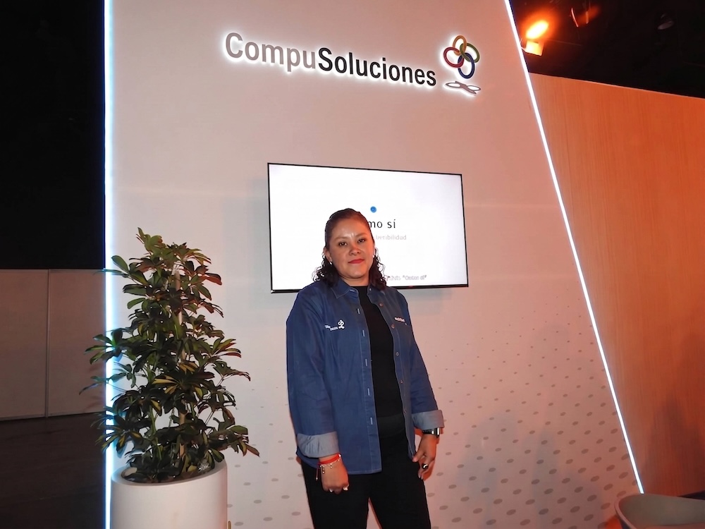 Fotografía de retrato corporativo en plano medio de Fabiola Munguía, Responsable de la Célula Dell Technologies dentro de CompuSoluciones, posando frente al estand con el logotipo de la empresa.