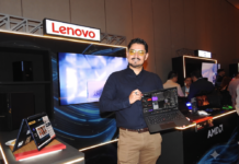 Lenovo y la fuerza de AMD revolucionan la tecnología desde el sector comercial al entretenimiento Fotografía en plano medio de Fernando Acevedo Mejía, Especialista de Preventa para Lenovo y AMD, sonriendo en el estand iluminado de las marcas mientras sostiene con una mano una computadora portátil ThinkPad abierta para mostrar su pantalla y software operativo.