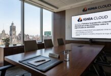 Ignia Cloud y Sendmarc se unen para blindar el correo corporativo frente al phishing Fotografía de una sala de juntas corporativa iluminada con vista hacia la Catedral Metropolitana de la Ciudad de México a través de un ventanal panorámico. En el centro de la mesa de madera pulida se observa una carpeta de piel con pluma de ejecutivo y una placa con el nombre "Esteban Rey - CEO". Al fondo, sobre una pared de madera, destaca una pantalla gigante con el logotipo de Ignia Cloud proyectando puntos clave sobre la protección del correo electrónico contra la suplantación de identidad.