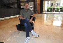 GPS revoluciona el modelo de ciberseguridad y transforma al canal de distribución Fotografía en plano medio de Jorge Durán, CEO y fundador de Grupo Propulsor de Soluciones (GPS) para Latinoamérica, vistiendo una playera polo color verde olivo, jeans y calzado deportivo, sentado con las piernas cruzadas en un sillón individual negro en el vestíbulo de un hotel.