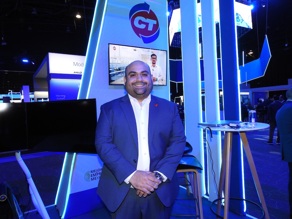 Fotografía en plano medio de Juan Pablo Rojo, Director Adjunto de Marcas en CT Internacional, luciendo un traje azul marino y sonriendo en el estand iluminado de la empresa.