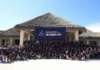 ¡Todo un éxito Anadic Mx The Summit 2026! Nadie es mejor que todos juntos Fotografía de un grupo multitudinario de personas posando alegremente sobre la arena blanca de una playa, frente a una gran estructura arquitectónica tipo palapa. La inmensa mayoría de los asistentes viste camisas tipo polo en color azul oscuro y, en el centro de la formación, sostienen una gran lona azul con el logotipo y el texto "ANADIC MX THE SUMMIT 2026". El día luce soleado con un cielo completamente despejado.