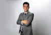Salicru identifica nuevas oportunidades para el canal en el mercado de protección energética Fotografía de retrato de Juan Carlos Casillas, vestido con un traje gris, camisa blanca y corbata oscura. Posando de pie, con los brazos cruzados y una ligera sonrisa, frente a un fondo blanco con iluminación de estudio.