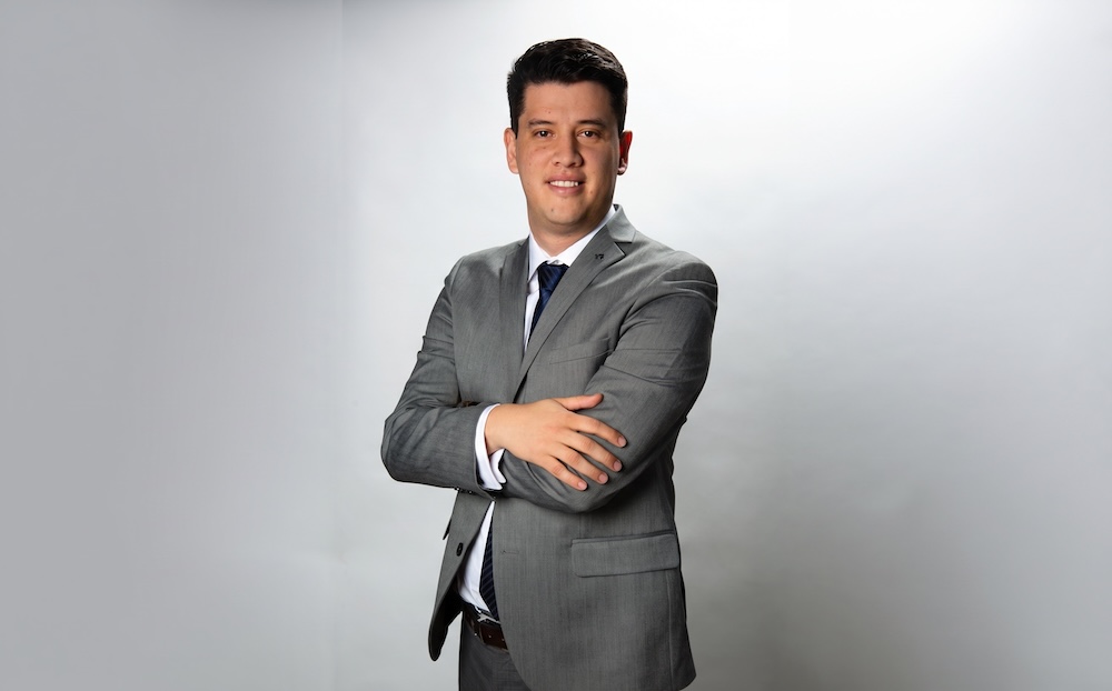 Liderazgo para la expansión del respaldo de energía en México Fotografía de retrato de Juan Carlos Casillas, vestido con un traje gris, camisa blanca y corbata oscura. Posando de pie, con los brazos cruzados y una ligera sonrisa, frente a un fondo blanco con iluminación de estudio.