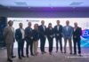 El futuro de la ciberseguridad: TEAM y SailPoint unen fuerzas para revolucionar la identidad digital Fotografía grupal de nueve ejecutivos e integrantes de los equipos de TEAM y SailPoint posando sonrientes en fila en una sala de eventos, frente a una pantalla gigante con gráficos de ciberseguridad e identidades digitales.