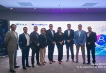 El futuro de la ciberseguridad: TEAM y SailPoint unen fuerzas para revolucionar la identidad digital Fotografía grupal de nueve ejecutivos e integrantes de los equipos de TEAM y SailPoint posando sonrientes en fila en una sala de eventos, frente a una pantalla gigante con gráficos de ciberseguridad e identidades digitales.