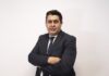 Grupo CVA nombra a Miguel Espinoza como CEO interino tras la salida de Moisés Avelar Fotografía de retrato corporativo de Miguel Espinoza posando de pie con los brazos cruzados y mirando al frente con una ligera sonrisa. Viste un traje formal de color azul marino, camisa blanca y corbata oscura con discreto patrón de lunares blancos, frente a un fondo blanco liso de estudio.