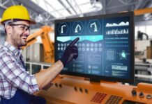 ViewSonic lanza en América Latina su nueva línea exclusiva de monitores táctiles industriales Open Frame Fotografía de un operador industrial con casco amarillo, lentes de protección y guantes negros de trabajo, sonriendo mientras toca con el dedo un panel HMI de automatización industrial que despliega esquemas de líneas de producción y gráficos de rendimiento.