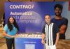 Innovación y tecnología con CONTPAQi para el impulso de las PyMEs Fotografía en plano medio de Nancy Torres y Brian Nishizaki sonriendo juntos a ambos lados de un módulo promocional de CONTPAQi con código QR y folletos institucionales.
