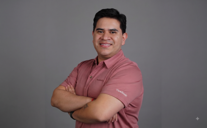 Pablo García impulsa la evolución de ViewSonic hacia un ecosistema de soluciones visuales Fotografía de retrato corporativo de Pablo García, Gerente Regional de Negocios para México en ViewSonic, luciendo una playera polo rosa con el logotipo grabado de la marca y los brazos cruzados sobre un fondo gris neutro.