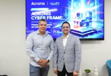 Licencias OnLine y Acronis Cyber Frame transforman el negocio de los proveedores de servicios Fotografía en plano medio de Salvador Rico, Distribution Account Manager para NOLA en Acronis, y Ernesto Jiménez, Country Sales Manager de Licencias OnLine, sonriendo juntos frente a una pantalla publicitaria de Acronis Cyber Frame.