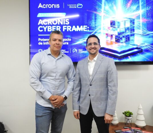 Licencias OnLine y Acronis Cyber Frame transforman el negocio de los proveedores de servicios Fotografía en plano medio de Salvador Rico, Distribution Account Manager para NOLA en Acronis, y Ernesto Jiménez, Country Sales Manager de Licencias OnLine, sonriendo juntos frente a una pantalla publicitaria de Acronis Cyber Frame.