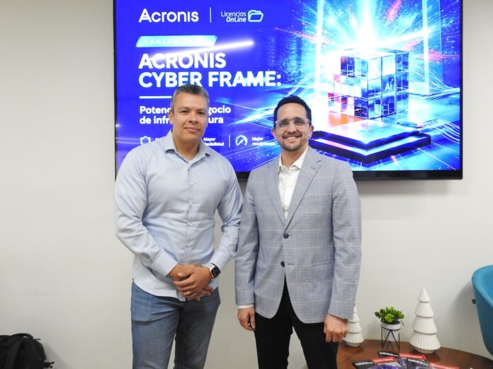 Salvador Rico y Ernesto Jiménez impulsan la alianza entre Acronis y Licencias OnLine en México Fotografía en plano medio de Salvador Rico, Distribution Account Manager para NOLA en Acronis, y Ernesto Jiménez, Country Sales Manager de Licencias OnLine, sonriendo juntos frente a una pantalla publicitaria de Acronis Cyber Frame.