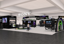 Sony revoluciona la producción en vivo e inmersiva en la feria IBC 2026 Renderizado arquitectónico en vista panorámica del estand de Sony en la convención IBC 2026, ubicado en un pabellón de convenciones con iluminación superior. La estructura negra destaca el lema "Creativity Connected" y el logotipo flotante iluminado de Sony en blanco, dividida en áreas temáticas como "News Production", "Live Production" y "Committed to Sustainability".