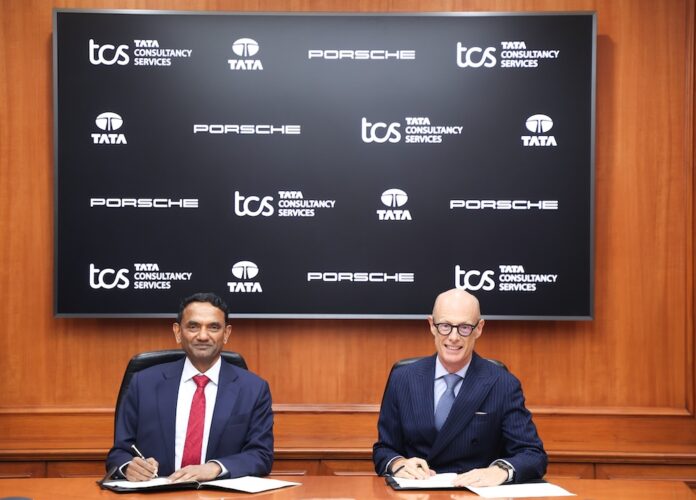 Fotografía institucional de K. Krithivasan y el Dr. Michael Leiters sentados en una mesa de reuniones de madera con bolígrafos en la mano para la firma de un documento corporativo. En el fondo se aprecia una pantalla que muestra repetidamente los logotipos oficiales de Tata Consultancy Services, TATA y Porsche.