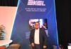 Exel del Norte transforma el ecosistema de canales mediante la inteligencia artificial y disponibilidad de inventario Fotografía en plano medio de Amador Rangel, Encargado de la gerencia de Dell Technologies cómputo en Exel del Norte, vistiendo un saco oscuro sobre una camisa blanca, posando sonriente frente a un muro azul con iluminación neón y la frase "EXEL, LO MEJOR EN TECNOLOGÍA PARA HACERTE CRECER".