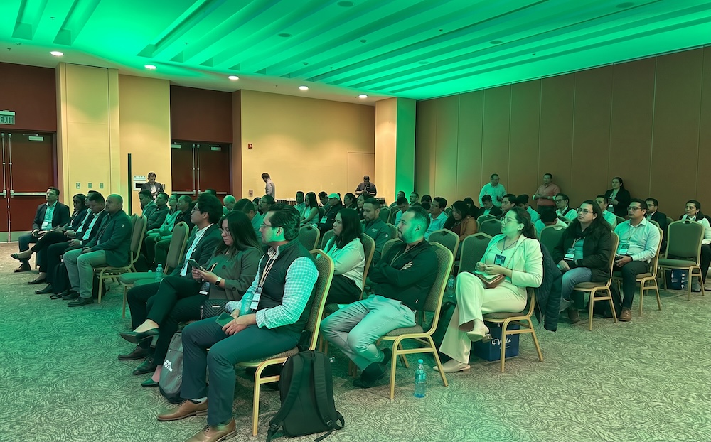 Fotografía en plano medio general del público asistente en el salón del Poliforum León, con iluminación verde ambiental, escuchando atentamente las ponencias del congreso.
