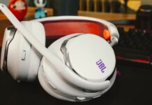 El sonido que sigue el ritmo de tus partidas: JBL renueva su línea Quantum Fotografía en plano detalle de los audífonos inalámbricos para videojuegos JBL Quantum 950 en color blanco con acentos morados y naranjas, mostrando su micrófono boom, la diadema de malla transpirable y las almohadillas descansando sobre un escritorio junto a un teclado mecánico.