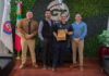 CT Internacional y Dahua fortalecen la distribución y continuidad operativa del canal en México Fotografía en plano entero de directivos de CT Internacional y Dahua Technology México posando de pie en sus oficinas corporativas con la bandera de México y sosteniendo una placa conmemorativa de madera como distribuidor autorizado.