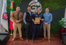 CT Internacional y Dahua fortalecen la distribución y continuidad operativa del canal en México Fotografía en plano entero de directivos de CT Internacional y Dahua Technology México posando de pie en sus oficinas corporativas con la bandera de México y sosteniendo una placa conmemorativa de madera como distribuidor autorizado.