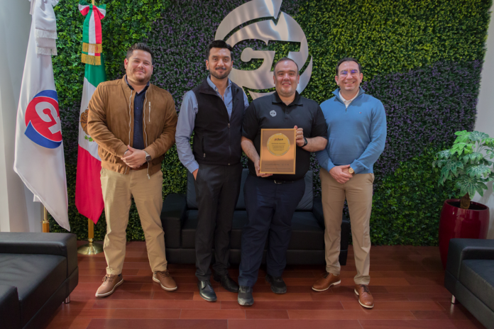 CT Internacional y Dahua Technology México fortalecen su alianza de distribución nacional Fotografía en plano entero de directivos de CT Internacional y Dahua Technology México posando de pie en sus oficinas corporativas con la bandera de México y sosteniendo una placa conmemorativa de madera como distribuidor autorizado.