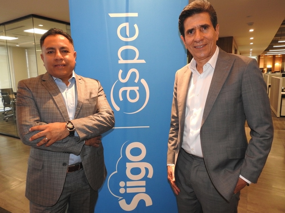Siigo Aspel y especialistas fiscales impulsan la profesionalización del canal ante la coyuntura laboral Fotografía en plano medio de Carlos Antonio Ibáñez y Eduardo Pérez posando juntos de pie sonrientes a los lados del pendón publicitario azul de Siigo Aspel.
