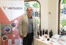Rentabilidad y nuevas oportunidades para el canal con las baterías de litio de Verbatim Fotografía de plano medio de Carlos Valdés, Country Manager de Verbatim México, posando junto a una mesa de exhibición con productos de la marca y un banner promocional corporativo.