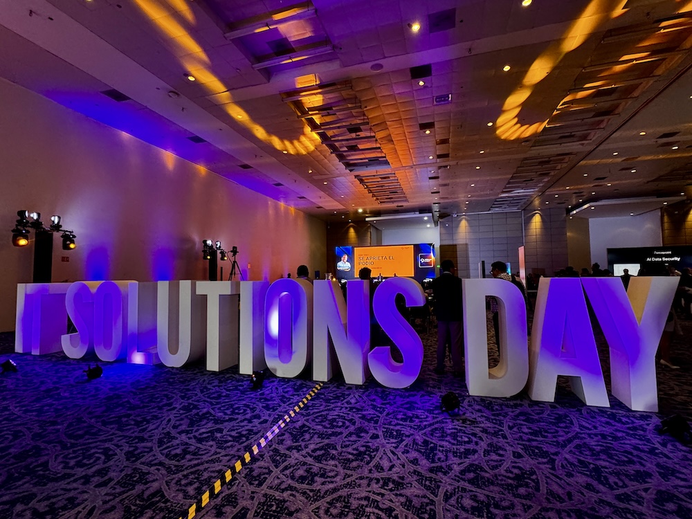 Fotografía en ángulo bajo que muestra un letrero volumétrico gigante con la frase IT SOLUTIONS DAY iluminado en tonos morados y azules en la entrada del salón de exposiciones del Centro Banamex.