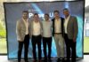 Innovación y expansión para el futuro en TD SYNNEX Power Up 2026 Fotografía de grupo de los cinco directivos principales de TD SYNNEX México —Jaime Venegas, Gerardo Calderón, Raffaelo Piccolo, Fabián Gómez y José Luis Chávez— posando abrazados y sonrientes frente a una mampara publicitaria azul de Power Up México 2026.