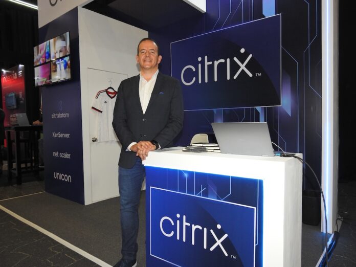Fabio Charry destaca la estrategia de gobernanza de datos y capas de acceso seguro de Citrix ante la IA Fotografía en plano medio de Fabio Charry, Partner Territory Manager para Centroamérica, México y el Caribe en Citrix, vistiendo un saco oscuro sobre camisa blanca y jeans, posando sonriente junto a un mostrador iluminado con el logotipo azul de Citrix.