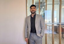 Streambe: Equipos más chicos y proyectos más baratos: el nuevo paradigma de programación que impulsa la IA Fotografía en plano medio de Gastón Gugliotta, CEO de Streambe, vistiendo un traje gris claro sobre camisa negra de vestir, posando sonriente en una oficina corporativa iluminada frente a un ventanal con mamparas de madera.