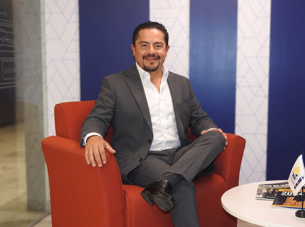 Fotografía de retrato en plano medio de Gerardo Romero, Director de Ingram Micro México, vistiendo saco gris sobre camisa blanca de vestir, sentado sonriente en un sillón rojo de sala de atención a clientes.