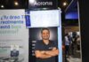 Acronis y el salto hacia la ciberseguridad impulsada por inteligencia artificial en Latinoamérica Fotografía de cuerpo medio de Guillermo Márquez, Solution Engineer Manager para Latinoamérica en Acronis, sonriendo con los brazos cruzados con una camiseta negra corporativa en un estand de exhibición frente a un monitor que muestra la interfaz de la plataforma y un cartel con la frase "¿Tu área TI realmente está bajo control?".