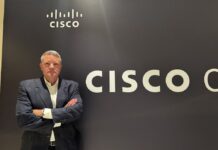 Cisco redefine las oportunidades y los retos para los socios de negocio en América Latina Fotografía de retrato en plano medio de Guy Diedrich, Senior VP y Global Innovation Officer de Cisco, vistiendo saco oscuro sobre camisa blanca, posando sonriente y con los brazos cruzados frente al muro con el logotipo corporativo de CISCO.