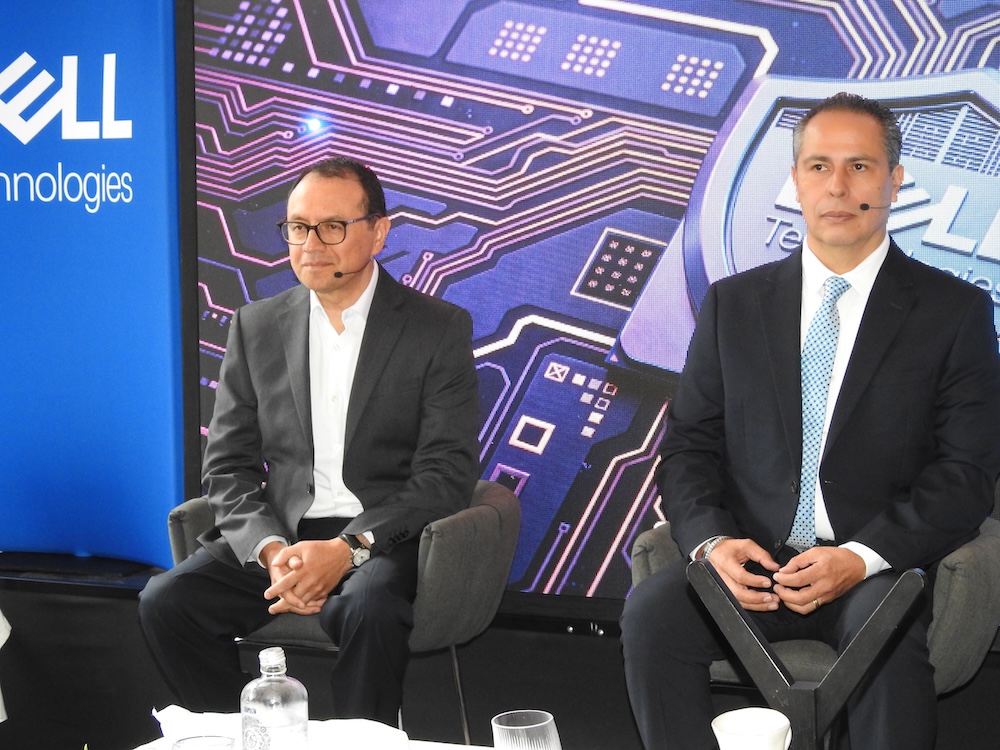 Fotografía en plano medio de Hiram Monroy, Director Comercial de Ventas de AMD, y Juan José Cisneros, Presidente de CISO Club, sentados en sillones de un panel de discusión frente a una pantalla LED con circuitos integrados.