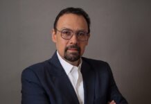 Tanium promueve la gestión activa de vulnerabilidades en el sector público y privado de México Fotografía de retrato en plano medio de Jorge López, Vicepresidente de Tanium Latinoamérica, vistiendo un saco azul marino sobre una camisa blanca de vestir, con anteojos y barba de candado, posando con los brazos cruzados frente a un fondo neutro gris.